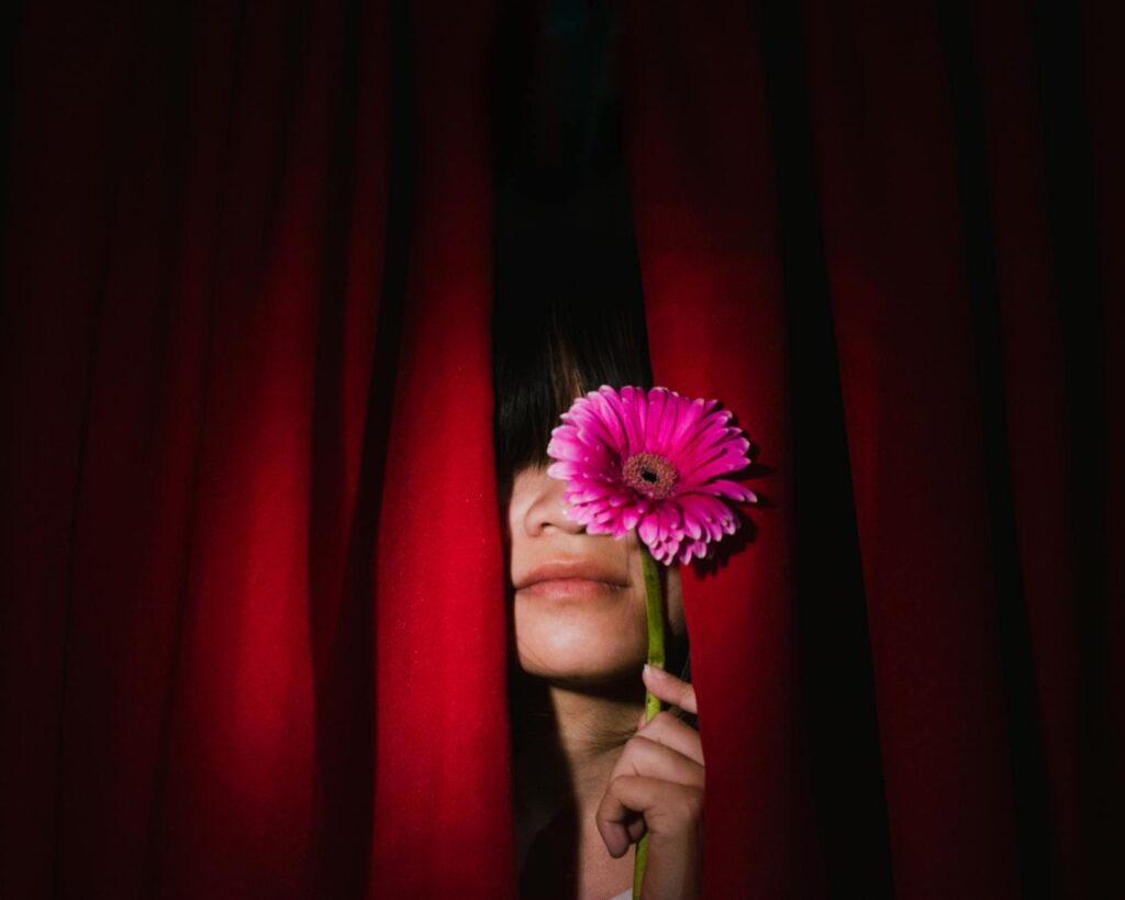 brunette woman posing behind red curtains with pink gerbera flower
